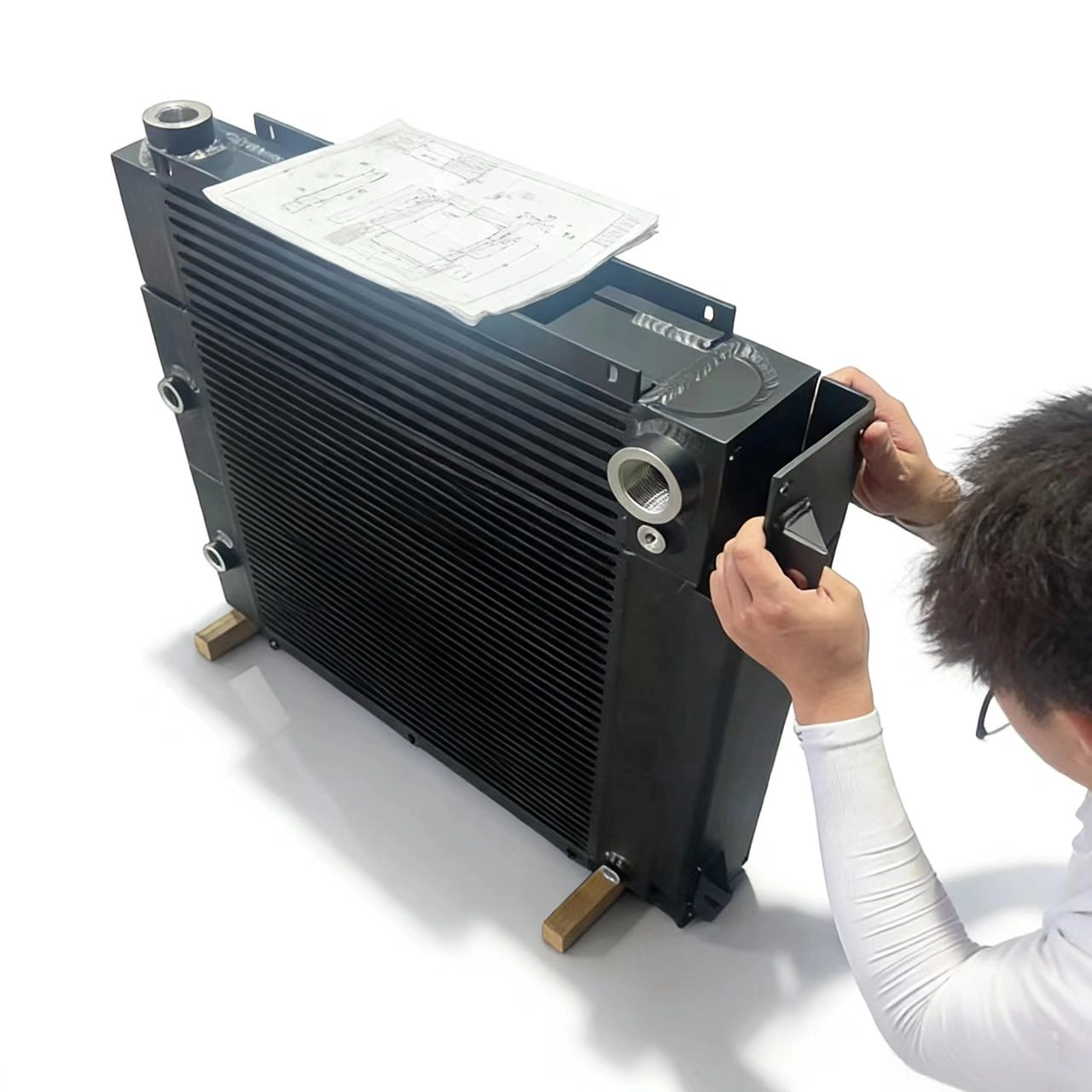 An engineer inspecting a custom black-coated bar and plate hydraulic oil cooler with technical drawing blueprint in an industrial workshop